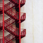 Red external emergency stairs on a white wall of a business building in downtown.