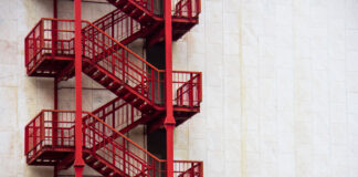 Red external emergency stairs on a white wall of a business building in downtown.