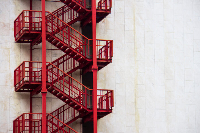 Red external emergency stairs on a white wall of a business building in downtown.