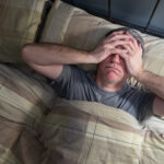 Man with insomnia lying in bed and snorting from exhaustion.