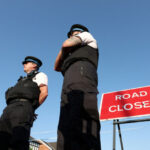 FILE PHOTO: Police officers stand near a "Road closed" sign, on the junction of Tithebarn Road and Hart Street, near the scene where a teenage suspect was arrested after people were stabbed in Southport